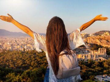 Frau steht über Athen und streckt die Arme im Sonnenuntergang aus. | © Adobe Stock/moofushi