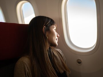 Junge Frau, die mit dem Flugzeug reist und aus dem Fenster schaut. | © GettyImages/FG Trade