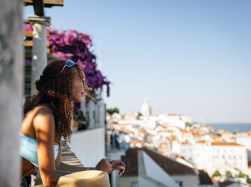 Junge Frau blickt von einem Balkon über Lissabon | © Getty Images/Westend61