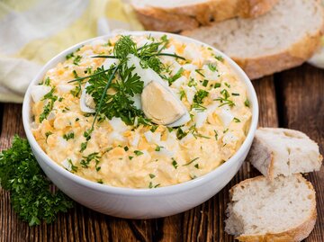Cremiger Eiersalat in einer weißen Schüssel steht neben Baguette auf dem Tisch. | © Getty Images / HandmadePictures