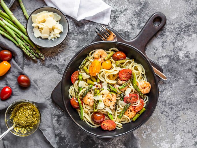 Ein Teller mit Spaghetti, grünem Spargel, Garnelen und frischen Kirschtomaten. | © Getty Images / Westend61