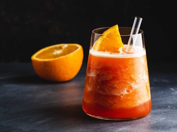 Eisgekühlter Frozen Aperol Sour steht auf einem Tisch vor einem schwarzen Hintergrund. | © Getty Images / nerudol