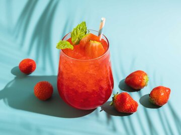 Ein erfrischendes Sommergetränk mit sprudelndem Effekt, geschmolzenem Eis, frischer Erdbeere und Trinkhalm sowie Minze in transparenten Gläsern auf einem blauen Hintergrund | © Getty Images/Redjina Ph