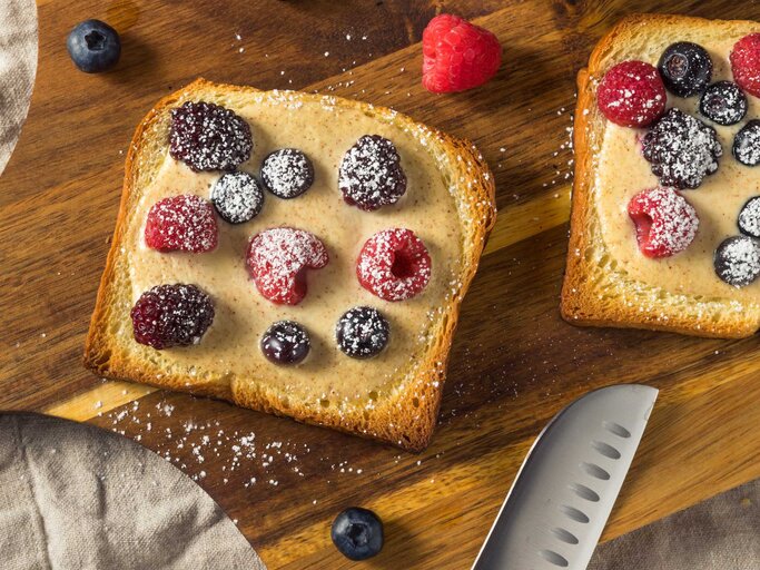 Hausgemachter trendiger Vanillepudding-Joghurt-Toast mit frischen Beeren auf einem Holzbrettchen serviert | © Getty Images/bhofack2