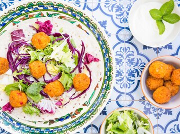 Ein bunt gefliester Tisch mit einer Schüssel Falafel, Salat und Joghurtsoße | © Getty Images/Westend61