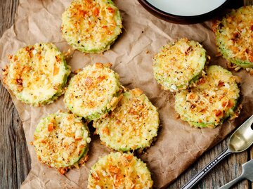 ebackene Parmesan Zucchini Chips auf dunklem Holzgrund | © Getty Images/nata_vkusidey