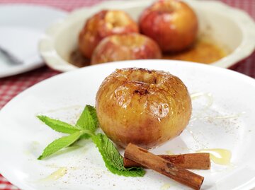 Bratapfel mit Dominosteinfüllung auf weißem Teller neben Pfefferminze und Zimtstangen | © GettyImages/wsmahar