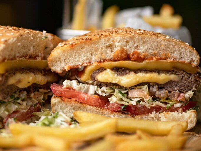 Aufgeschnittener Cheeseburger mit Pommes | © Getty Images/Artur Kozlov