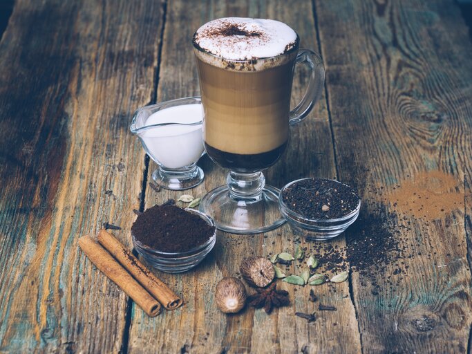 Chai Latte serviert mit Kakao, Zimt und Milch auf einem Holztisch | © Getty Images/Uladzimir Zuyeu