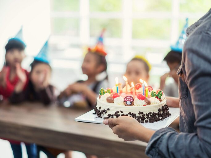 Frau bringt Geburtstagstorte an Kindertisch | © Getty Images/Prasit photo