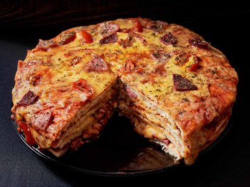 Italienischer Pizzakuchen mit vier Lagen voller gegrillter Salami, Schinken und Käse | © Getty Images/Maya Malkova