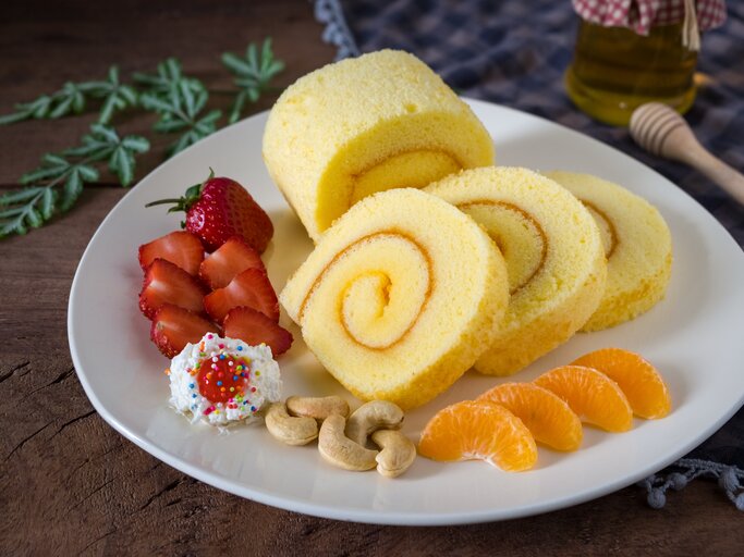 Zitronenrolle mit Erdbeeren, Erdnüssen und Mandarinen auf einem Teller | © Getty Images/Sirintra Pumsopa