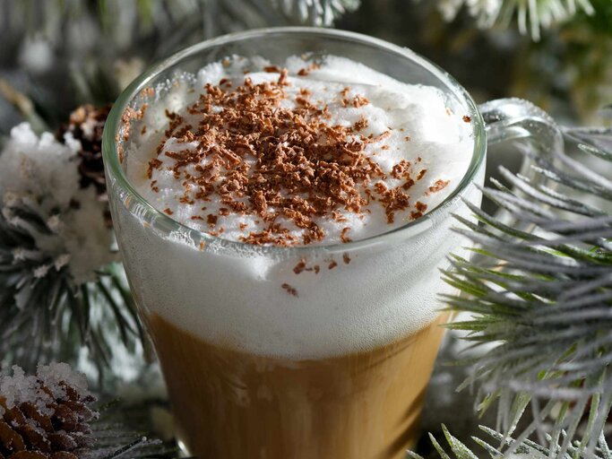 Weihnachtlicher Latte Macchiato. Ein tolles heißes Kaffeegetränk mit Schokoladenspänen, zwischen den schneebedeckten Kiefernzweigen und Schnee | © Getty Images/MarynaVoronova