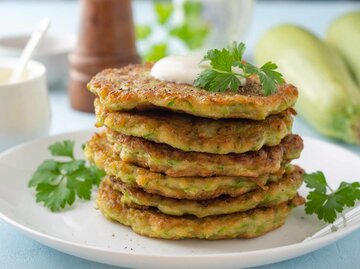 Zucchini-Puffer mit frischer Petersilie und saurer Sahne auf einem Teller | © Getty Images/Andrey Zhuravlev