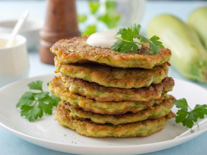 Zucchini-Puffer mit frischer Petersilie und saurer Sahne auf einem Teller | © Getty Images/Andrey Zhuravlev