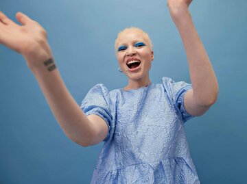 Frau mit Piercings und blondierten Haaren freudig vor blauer Wand | © Getty Images/Klaus Vedfelt