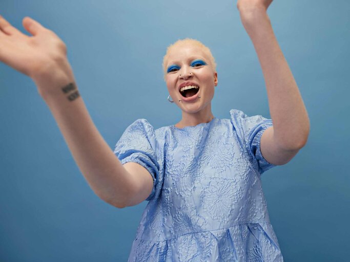 Frau mit Piercings und blondierten Haaren freudig vor blauer Wand | © Getty Images/Klaus Vedfelt