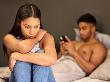 Eine junge Frau sieht traurig aus und ein junger Mann ist am Handy | © GettyImages/PeopleImages
