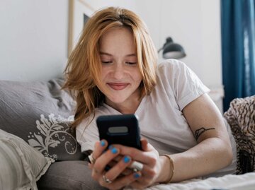 Junge Frau blickt lächelnd auf ihr Telefon. | © Getty Images/Willie B. Thomas