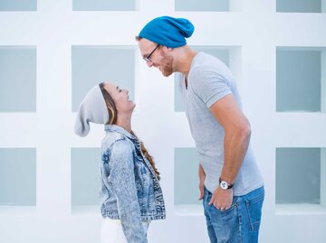 Paar mit großem Größenunterschied trägt jeweils eine Mütze und steht sich gegenüber.  | © Getty Images / Westend61
