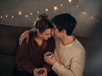 Frau und Mann sitzen Arm in Arm mit Kaffeetassen in den Händen auf dem Sofa | © AdobeStock/Jacob Lund