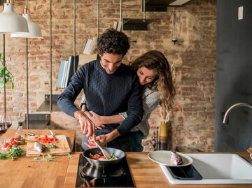 Pärchen kocht gemeinsam und umarmt sich in der Küche | © Getty Images/Arno Images