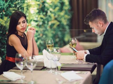 Frau schaut genervt beim Date, während ihr Partner sein Handy benutzt | © Getty Images/SrdjanPav