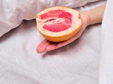 Frau hält eine Grapefruit im Bett. | © Adobe Stock/Iuliia Pilipeichenko