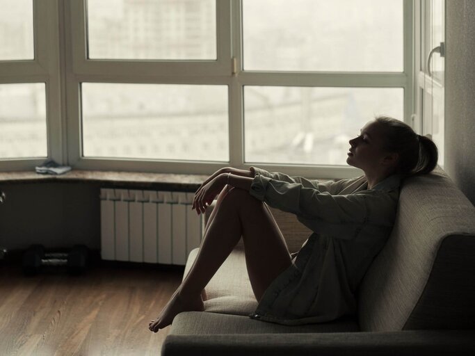 Person sitzt allein auf Sofa vor Fenster | © Getty Images/Igor Ustynskyy