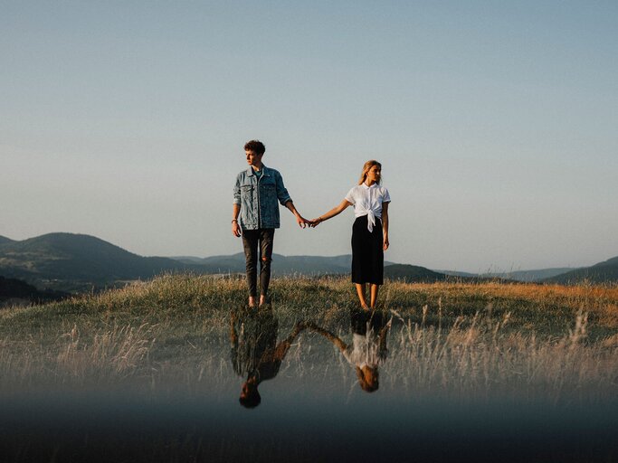 Junges Paar hält sich auf Abstand an der Hand und sieht voneinander weg. | © Getty Images/Halfpoint