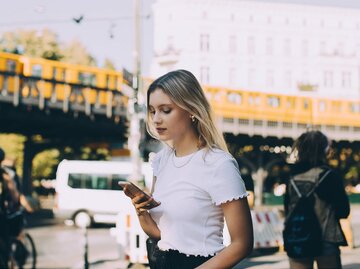 Frau steht auf der Straße und schaut auf ihr Handy | © Getty Images/Maskot