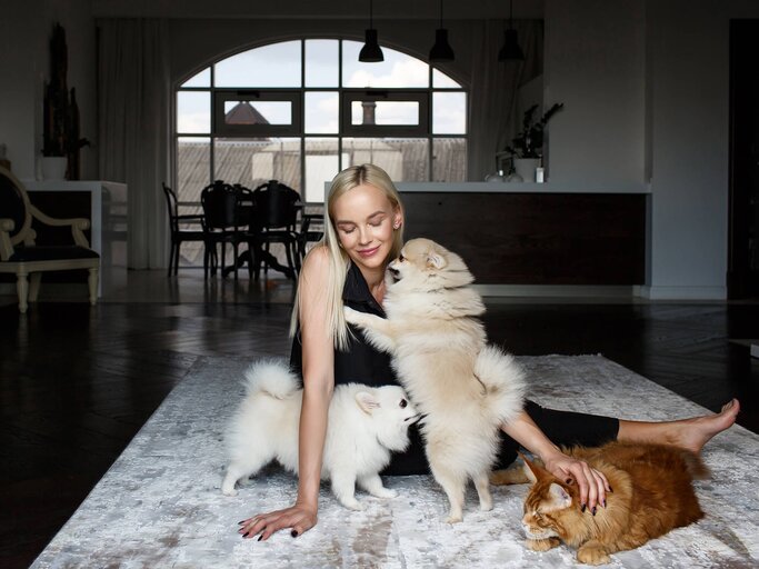 Frau mit Katze und Hunden sitzt auf dem Boden | © Getty Images/Victor Dyomin