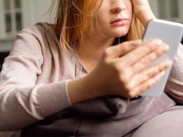 Frau schaut deprimiert auf ihr Handy | © Getty Images/Alexander Medvedev