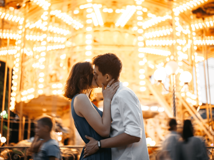 Frau und Mann küssen sich vor Karussell | © Getty Images/Igor Ustynskyy