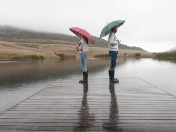 Paar steht mit Regenschirmen und Rücken an Rücken im Regen | © Getty Images/Westend61