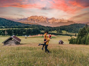 Junges Paar auf einer Wiese vor Bergen und Sonnenuntergang | © Getty Images/ljubaphoto