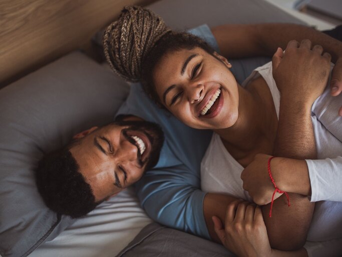 Paar liegt gemeinsam im Bett und lacht | © Getty Images/Halfpoint Images
