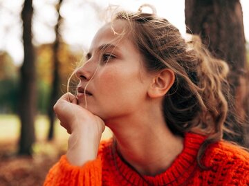 Nahaufnahme einer Frau, die einen orangenen Pullover trägt und in Gedanken versunken ist | © shutterstock/Yuricazac