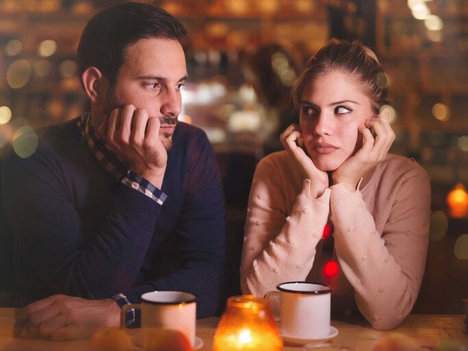 Mann und Frau sitzen an einer Bar und schauen sich genervt an