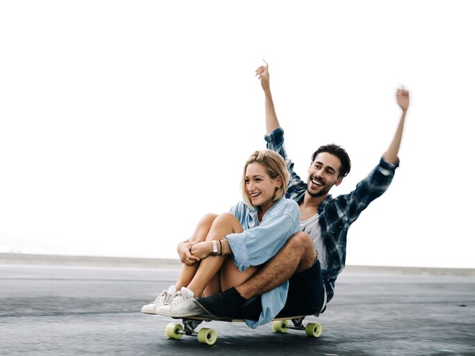 Frau und Mann fahren sitzend auf Skateboard | © Getty Images/Westend61