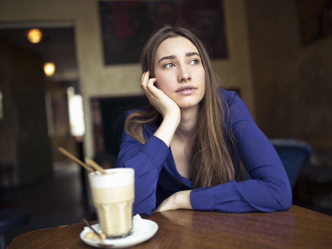Junge Frau sitzt im Cafe und schaut nachdenklich aus dem Fenster | © Getty Images/Westend61