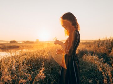 Frau steht bei Sonnenuntergang einsam auf einem Feld | © Getty Images/Igor Ustynskyy