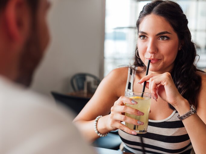 Frau sitzt mit ihrem Date im Cafe und trink ein Getränk während sie ihr Date anschaut | © Getty Images/MANICO