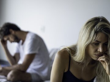 Junges Paar sitzt nachdenklich mit dem Rücken zueinander im Bett  | © Getty Images/PhotoAlto/Frederic Cirou