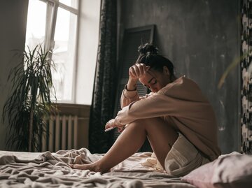 Junge Frau sitzt traurig und frustriert auf ihrem Bett | © Getty Images/Ol'ga Efimova/EyeEm