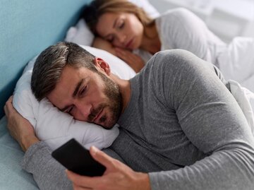 Frau schläft neben Mann am Handy im Bett. | © Getty Images/EmirMemedovski