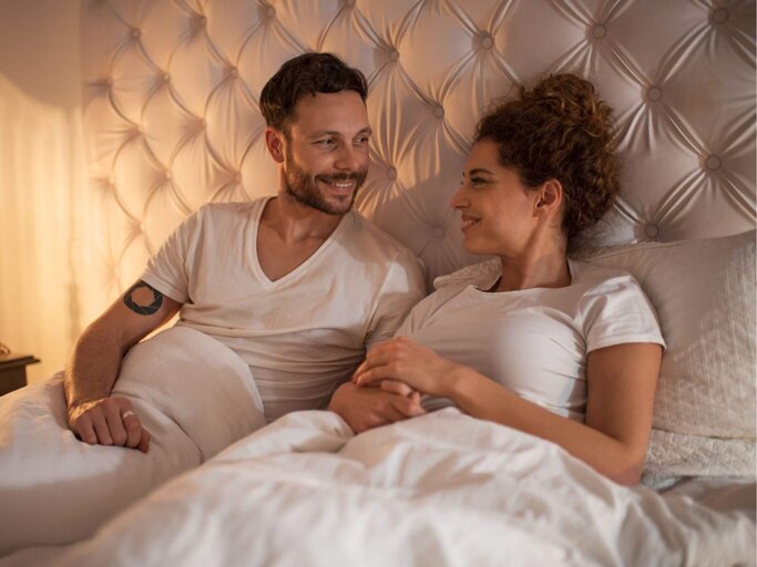 Frau und Mann sitzen im Bett und unterhalten sich | © Getty Images/BraunS