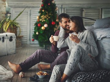 Frau und Mann in Pyjamas vor Weihnachtsbaum | © Getty Images/gilaxia