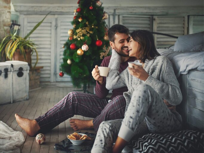 Frau und Mann in Pyjamas vor Weihnachtsbaum | © Getty Images/gilaxia