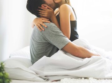 Frau sitzt im Bett dem Mann zugewandt auf seinem Schoß und küsst ihn leidenschaftlich. | © Getty Images / Witthaya Prasongsin